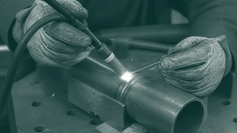 Unas manos con guantes de cuero sueldan un tubo metálico y saltan chispas