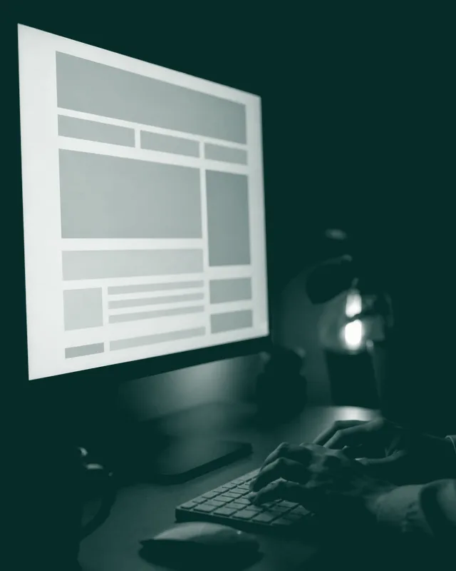 Una pantalla con el boceto de una web en construcción sobre un escritorio a oscuras, con un teclado delante