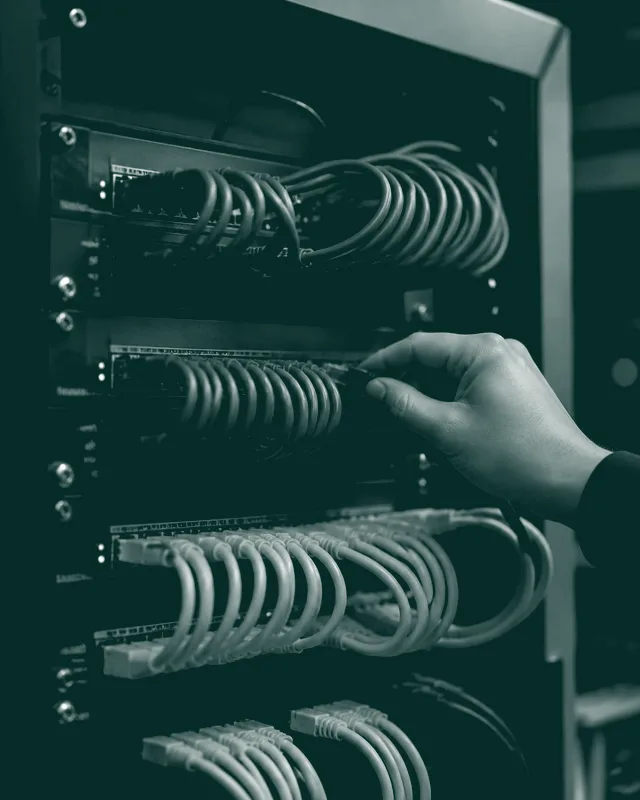 Una mano conecta un cable en un armario de red lleno de cables ordenados